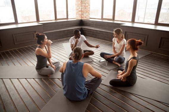 African-american yoga instructor talking to diverse group sitting on mat