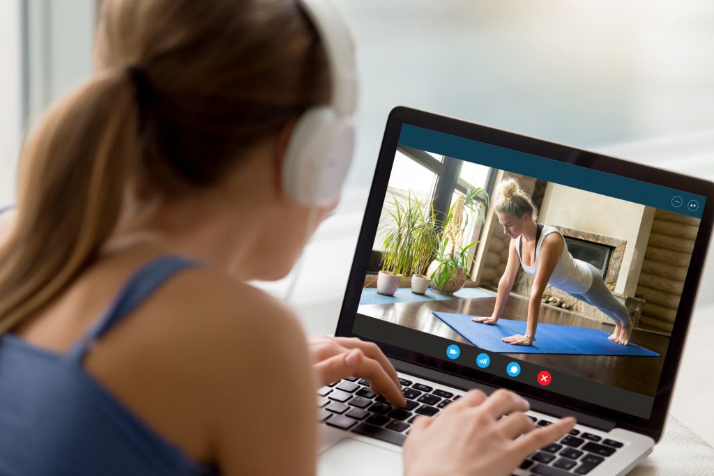 A girl with headphones on watching a yoga video on her laptop