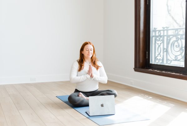 Katie sitting in a mindful pose in front of a laptop on a yoga mat