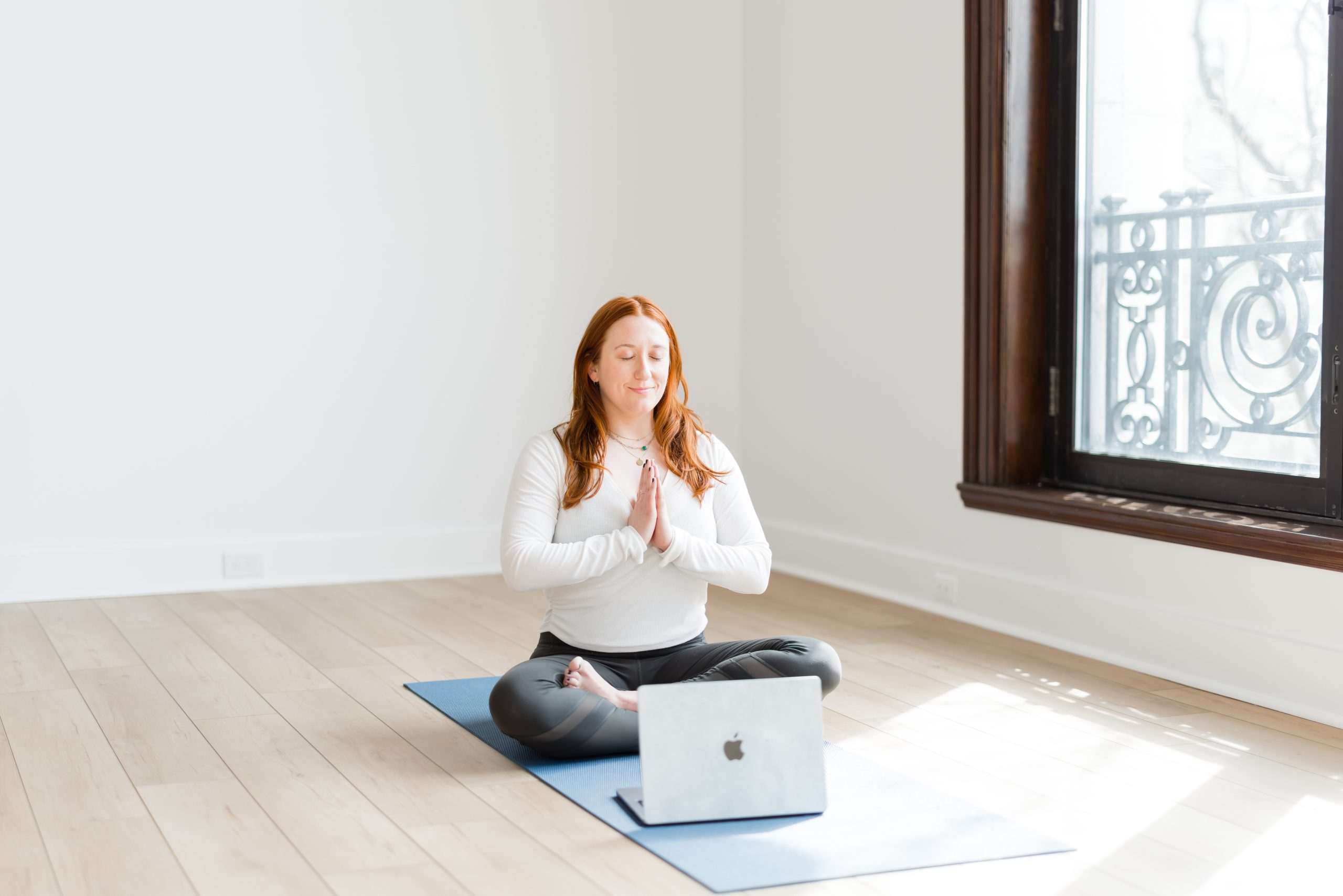 Katie sitting in a mindful pose in front of a laptop on a yoga mat