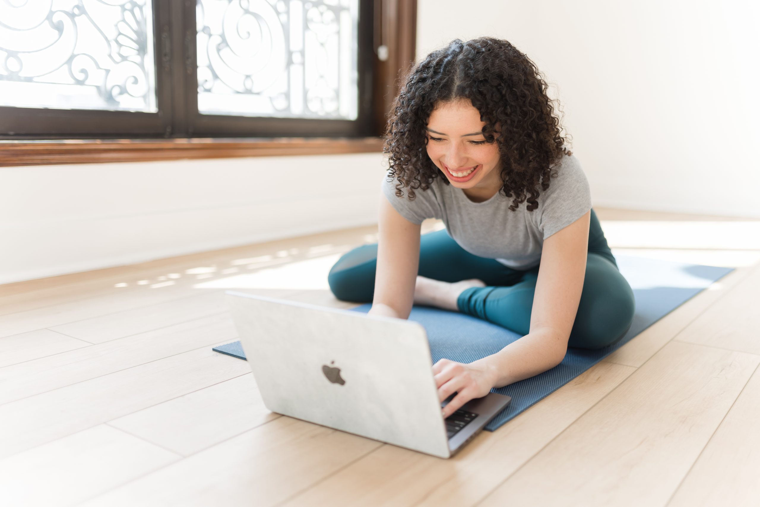 Girl enrolled in an online yoga teacher training program, using her laptop on a yoga mat