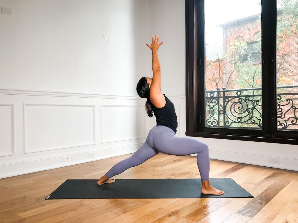 Person in Warrior I on a black yoga mat with arms up overhead