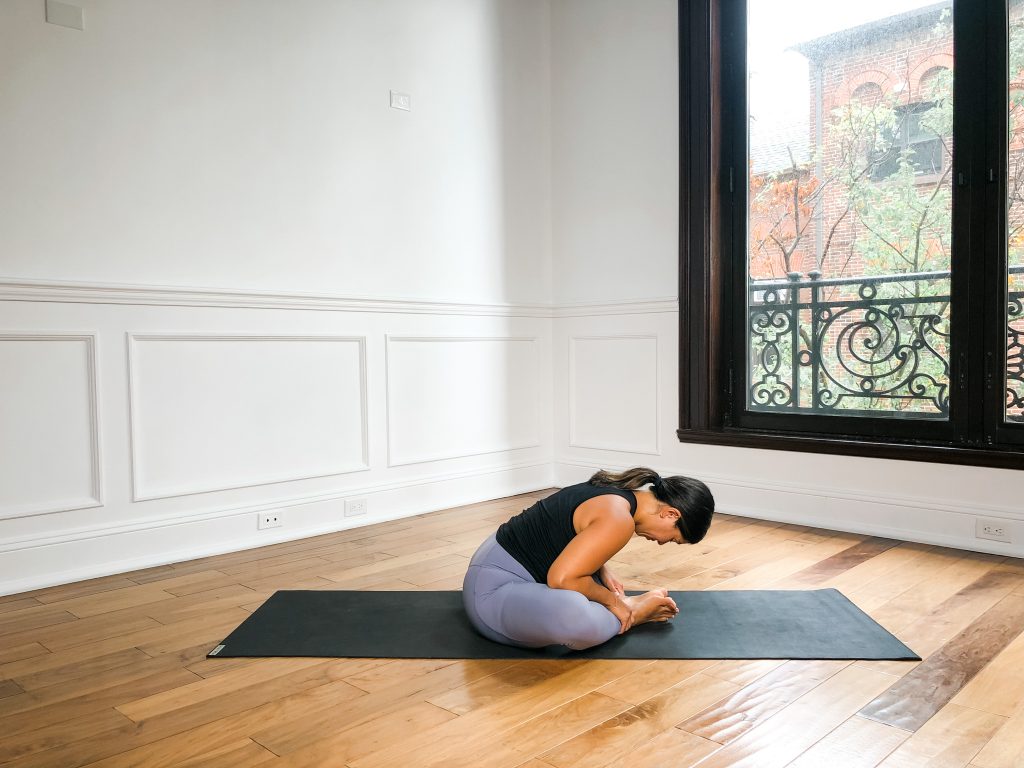 Yogi on a black yoga mat in Bound Angle Pose (Baddha Konasana)