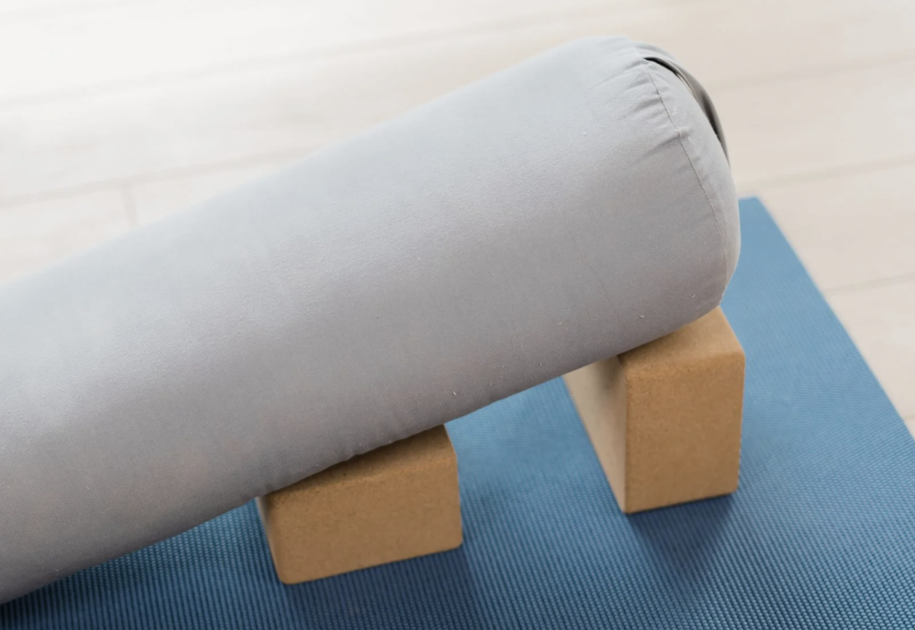 Yoga bolster resting on two blocks on top of a yoga mat