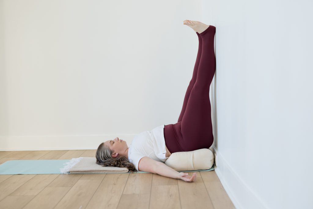 Alex lying on the ground with bolster beneath her sacrum and legs up against the wall
