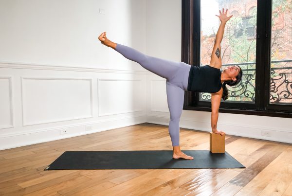 Person in Half Moon pose with their left hand on a block, right arm raised, on a black yoga mat