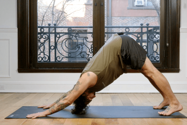 Man in a perfect down dog pose on a yoga mat in front of windows