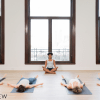 Yoga teacher sitting in front of a class in Sukasana while the students lie down in Savasana