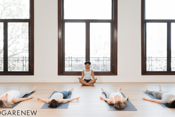 Yoga teacher sitting in front of a class in Sukasana while the students lie down in Savasana