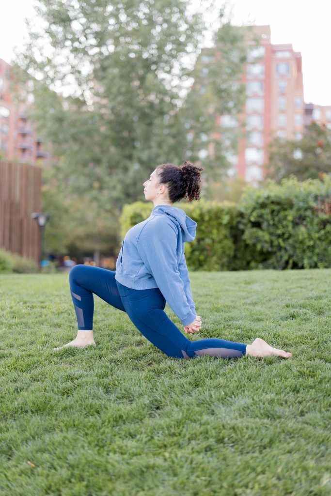Anjaneyasana pose on the grass outside with woman's hands clasped behind her back