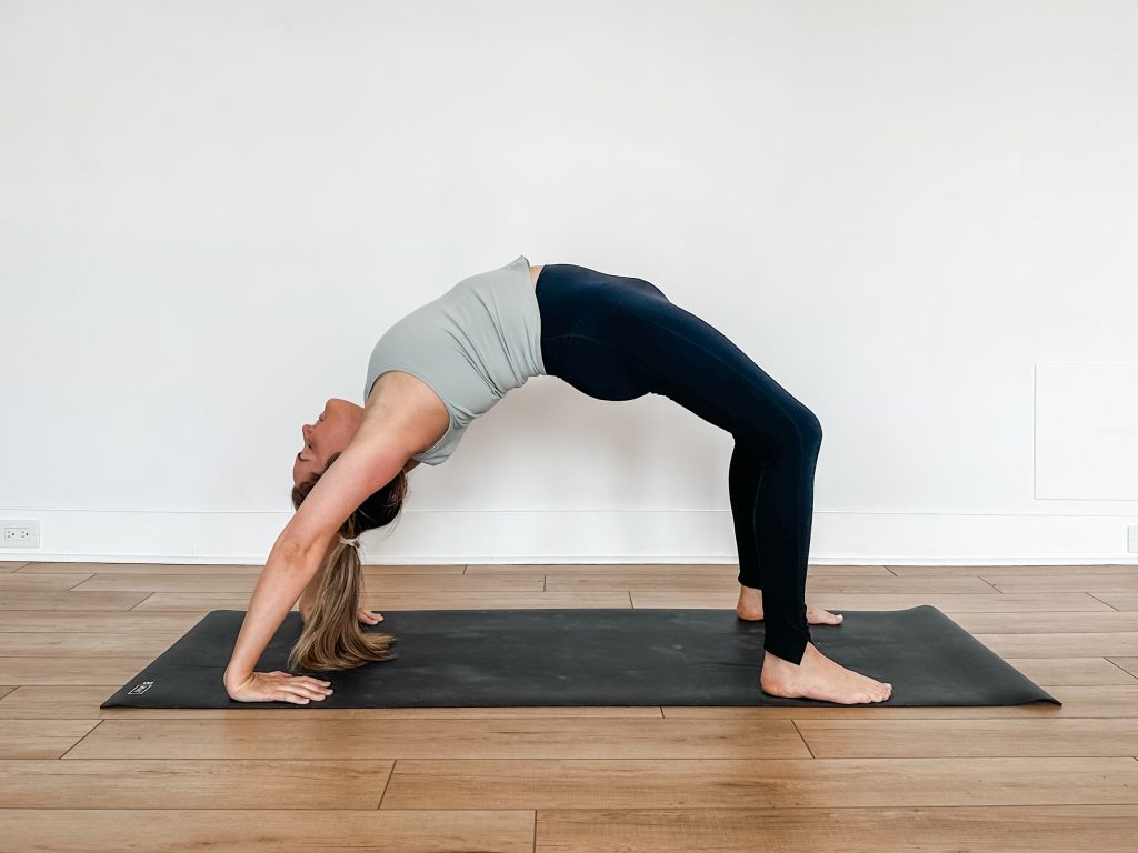 Woman in full wheel pose on a black yoga mat