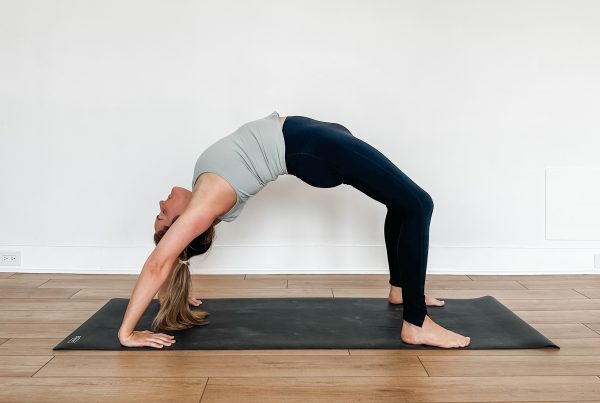 Woman in full wheel pose on a black yoga mat