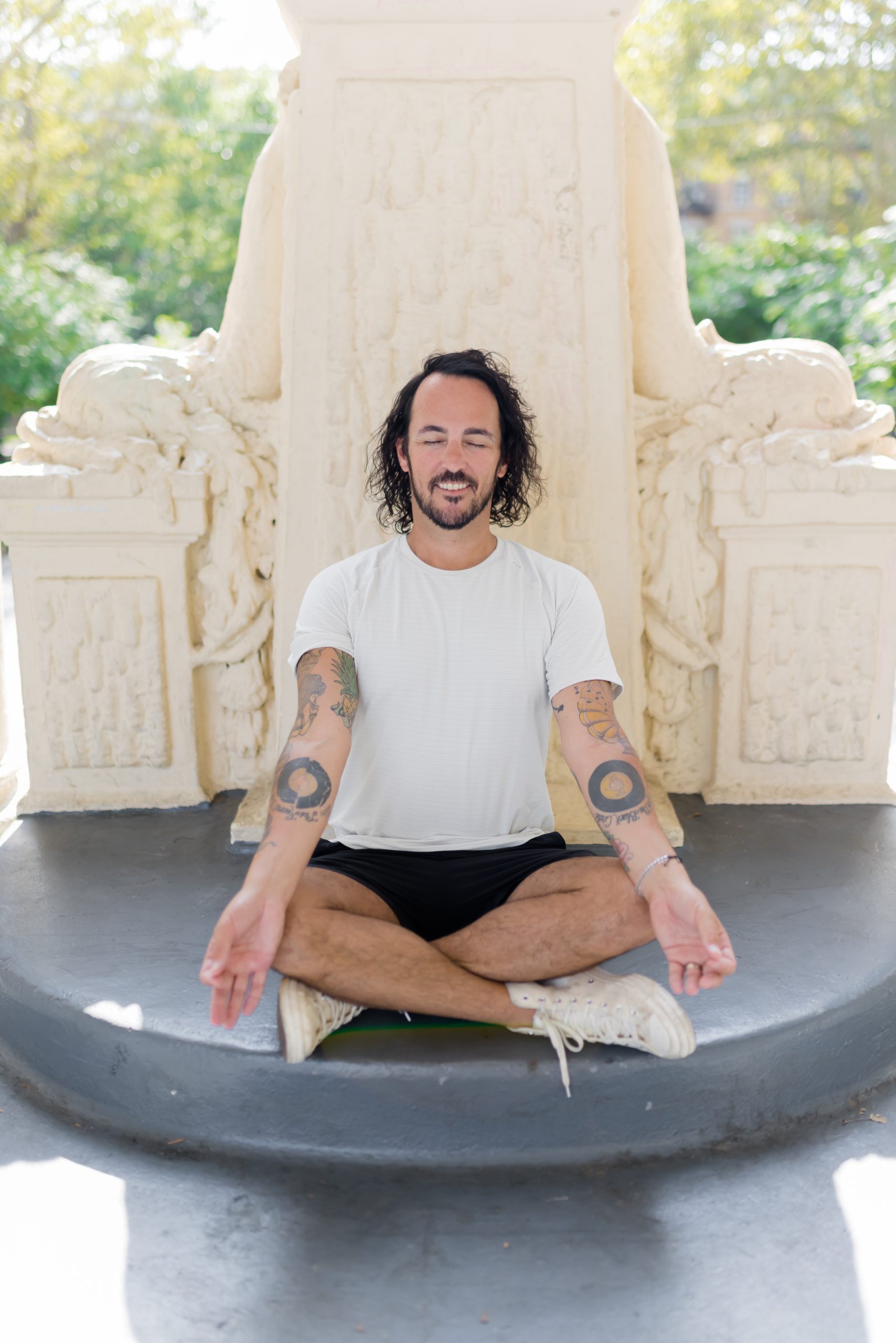 Patrick Franco of YogaRenew sitting in sukhasana in front of a beautiful ivory, stone sculpture in Hoboken, NJ