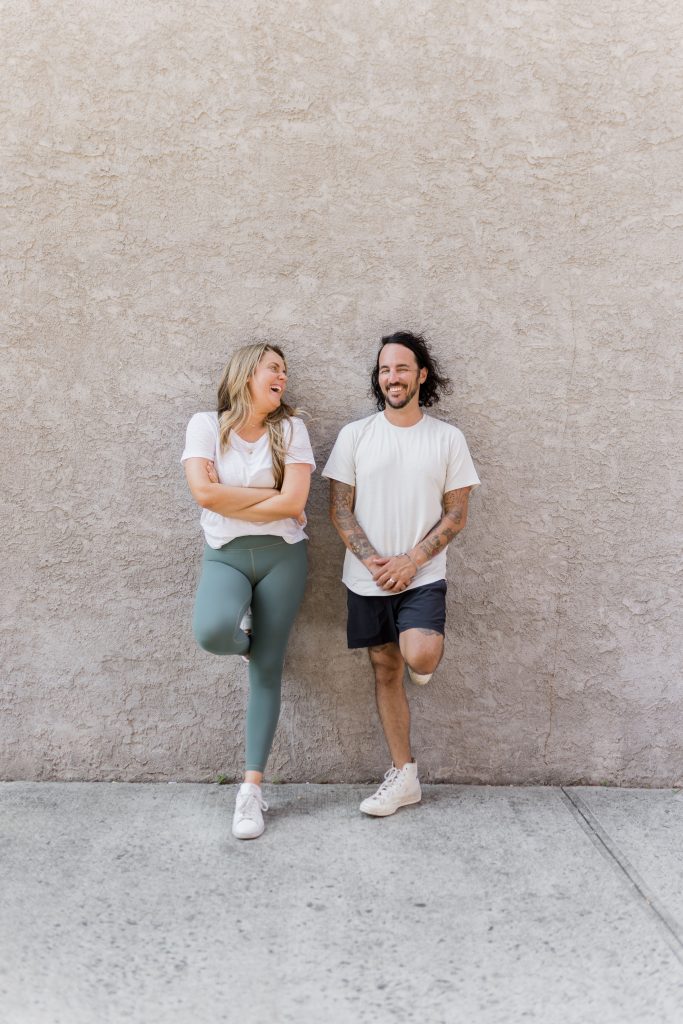 Kate & Patrick standing against a cement wall for the Vinyasa Yoga Sequencing Course photoshoot