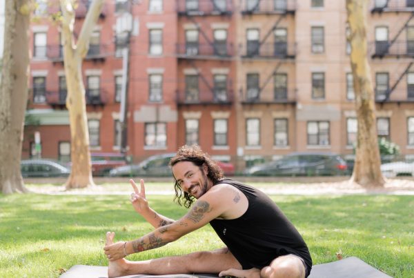 Patrick Franco in the grass on a yoga mat throwing up the peace sign