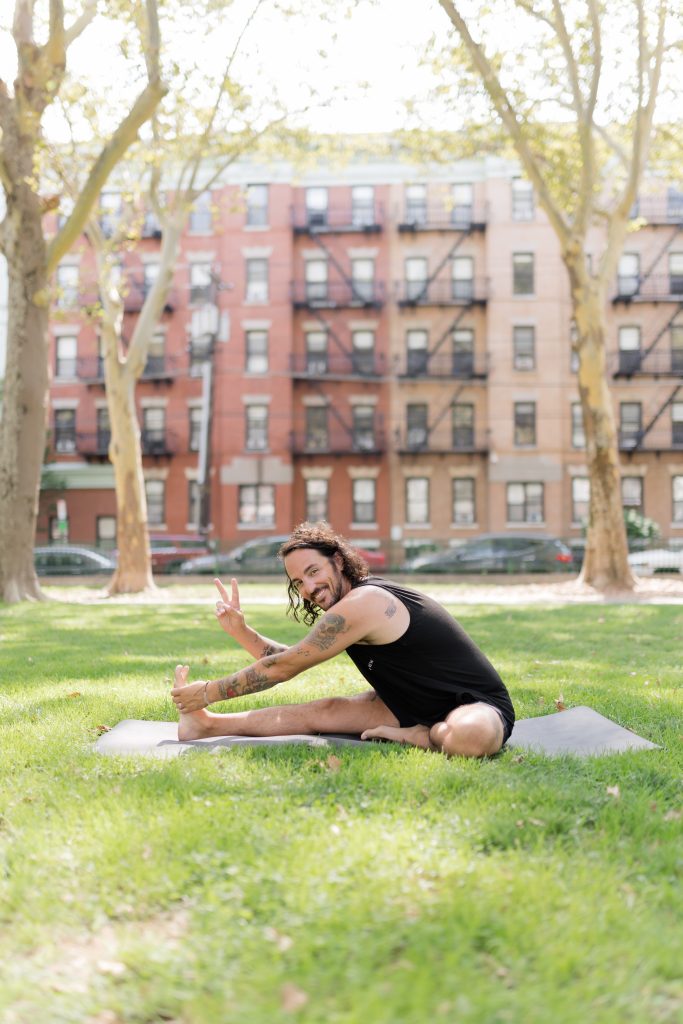 Patrick Franco in the grass on a yoga mat throwing up the peace sign