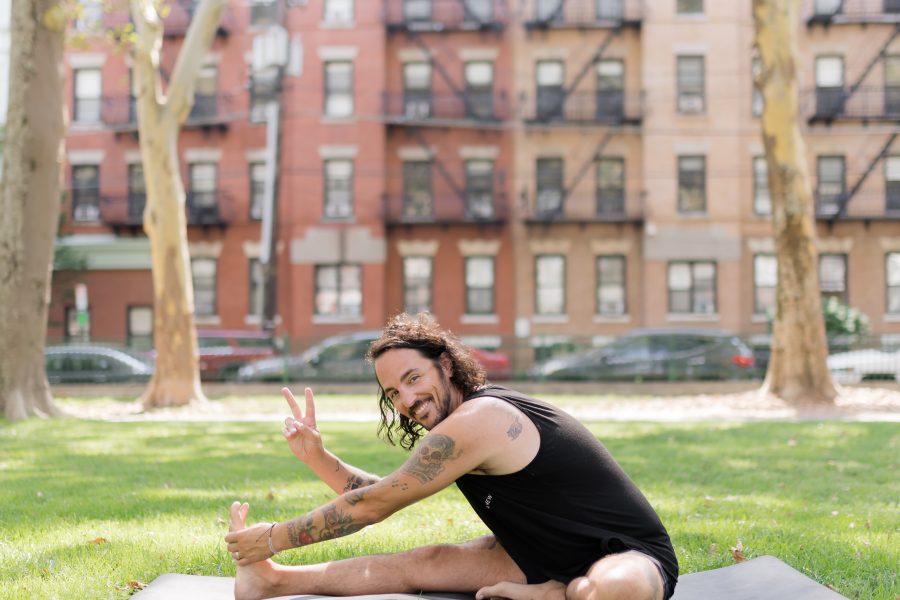 Patrick Franco in the grass on a yoga mat throwing up the peace sign