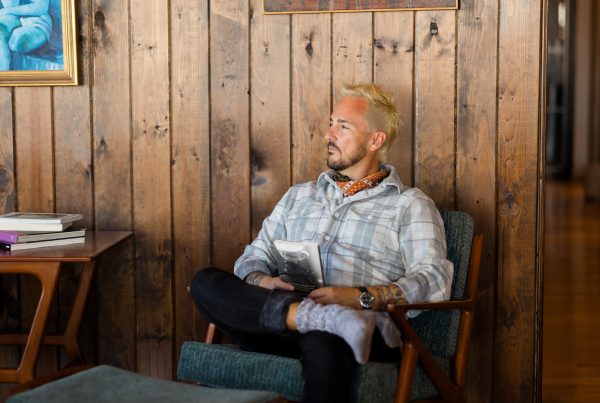 Patrick Franco sitting in a cozy chair, looking down on his reflections from the year in a wood cabin with cool art hanging behind him