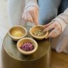 Ayurveda herbal powders and leaves with hands touching a small bowl of fennel