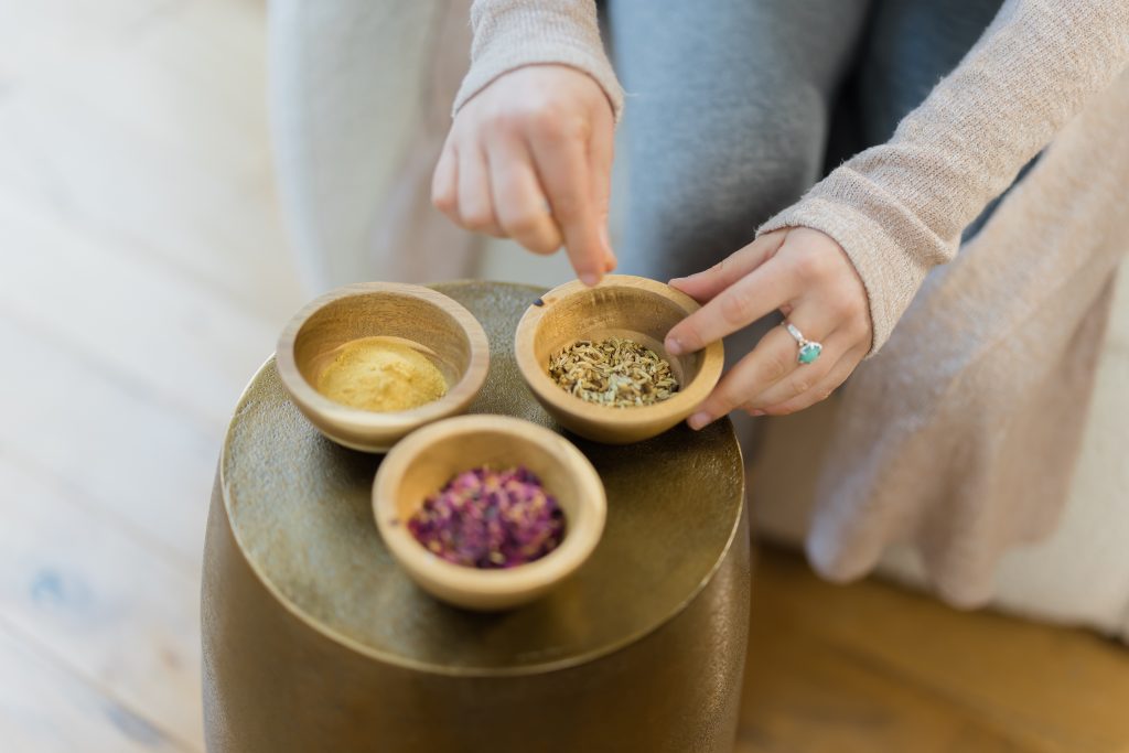 Ayurveda herbal powders and leaves with hands touching a small bowl of fennel