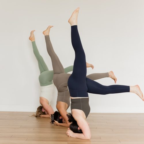 3 yogis in headstand with one leg lowered and one raised