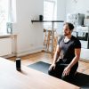 Yogi sitting in Virasana on a yoga mat following instructions from an AI voice assistant like Alexa or Siri from a speaker sitting on a table in front of them