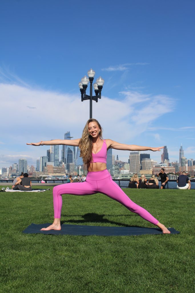Carlie in Warrior 2 in front of the NYC skyline in Hoboken, NJ