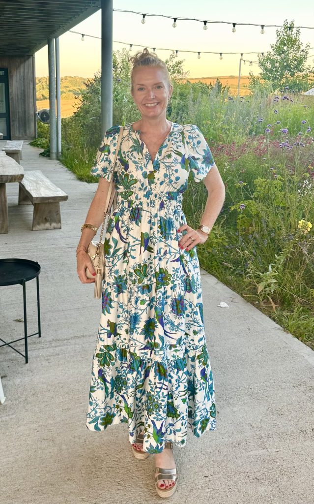 Joanne Silver in a floral dress, smiling, with her hand on her hip