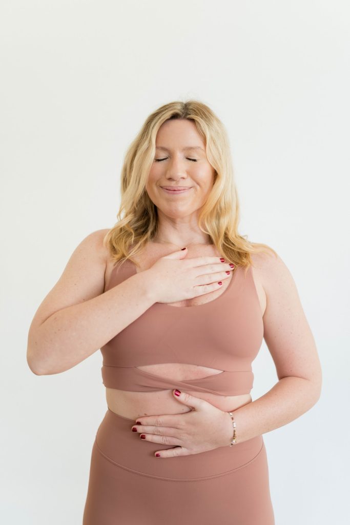 Emma O'Connor with one hand on her belly, one hand on her heart, eyes closed, gently smiling