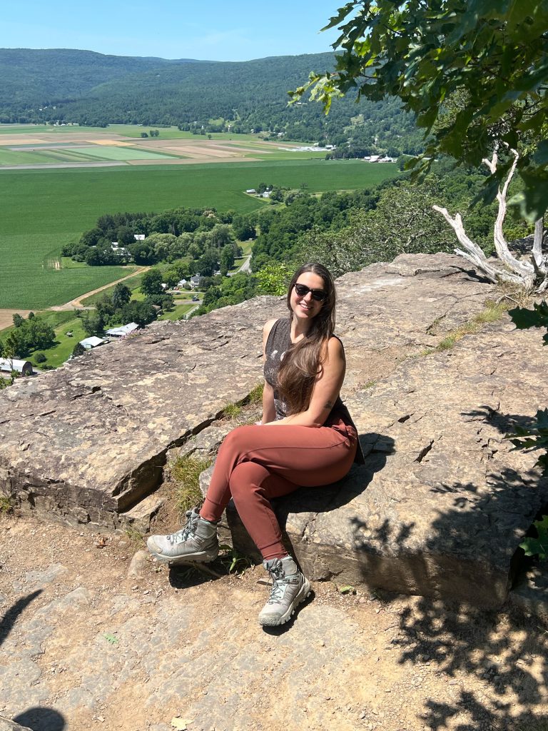 Lucianna Silvestri sitting crossed legged on a rock with sunglasses on, smiling at the camera