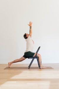 Man in Warrior 1 yoga pose using a chair